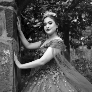 Quincea&ntilde;era in a long gown posing beside a stone column in soft evening light
