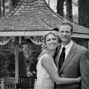 Bride embracing the groom while posing together in front of a wooden gazebo on their wedding day