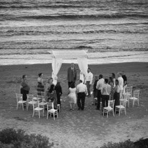 Wide view of a beach wedding ceremony under a simple arch with guests seated in rows